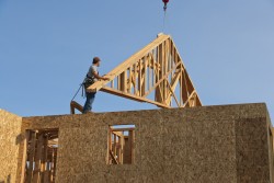 Crane hoisting roof trusses onto the unfinished frame of a residential home.